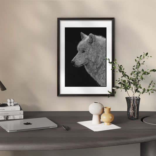 Zeichnung aus weiß und Grautönen eines Wolfskopfes auf schwarzem Papier mit dunklem Rahmen an der Wand über einem Schreibtisch